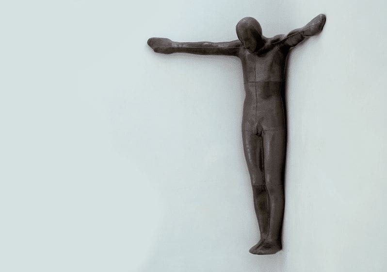 Sculpture of human figure in the corner of a corner of a room with arms outstretched.