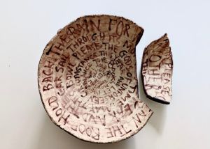A stoneware bowl covered in writing deliberately broken into two parts to resemble a museum relic