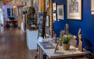 Image shows craft gallery at The Burton, tables with ceramics and art on the walls