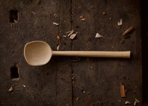 Image shows carved wooden spoon lying on a wooden table
