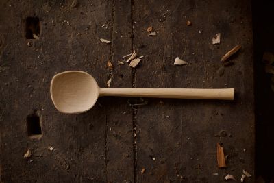 Image shows carved wooden spoon lying on a wooden table