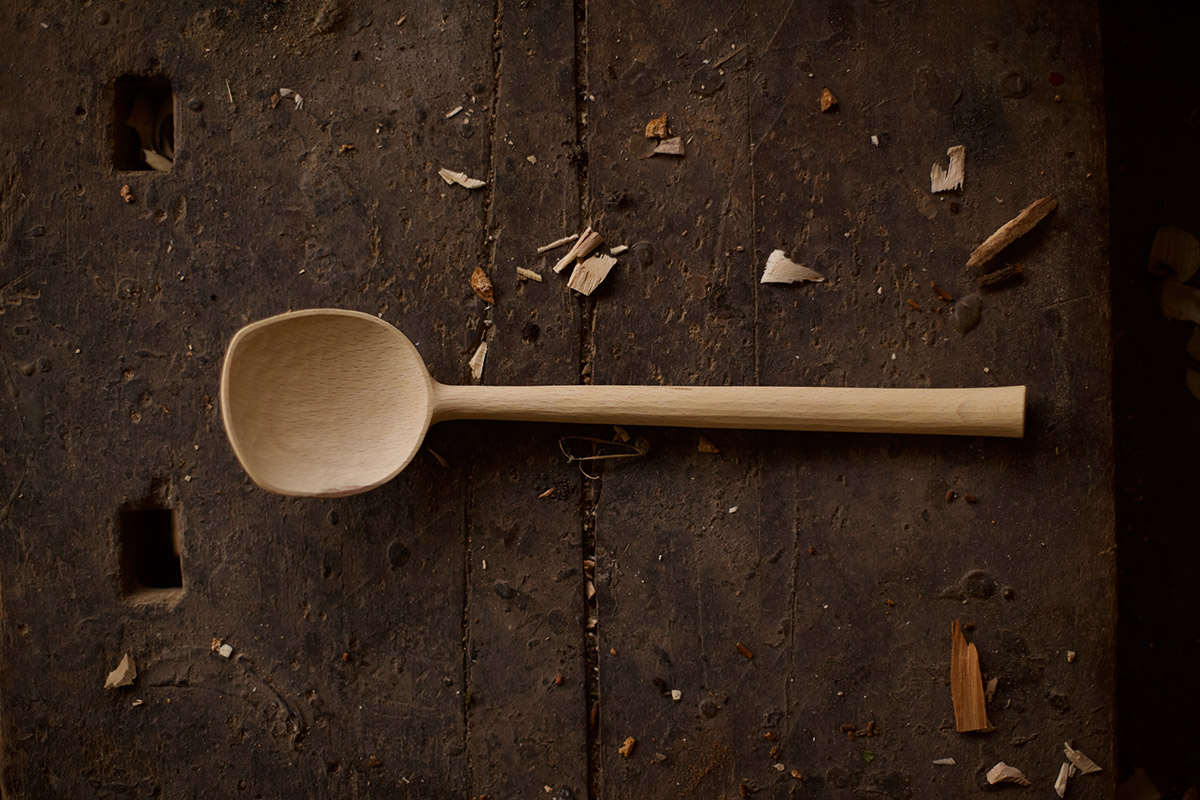 Image shows carved wooden spoon lying on a wooden table