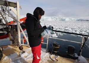 Image shows Emma Stibbon drawing on deck of ship surrounded by icebergs