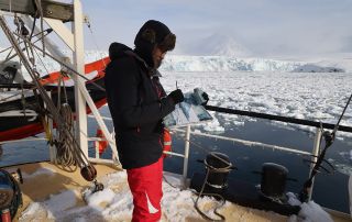 Image shows Emma Stibbon drawing on deck of ship surrounded by icebergs