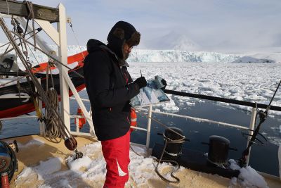 Image shows Emma Stibbon drawing on deck of ship surrounded by icebergs
