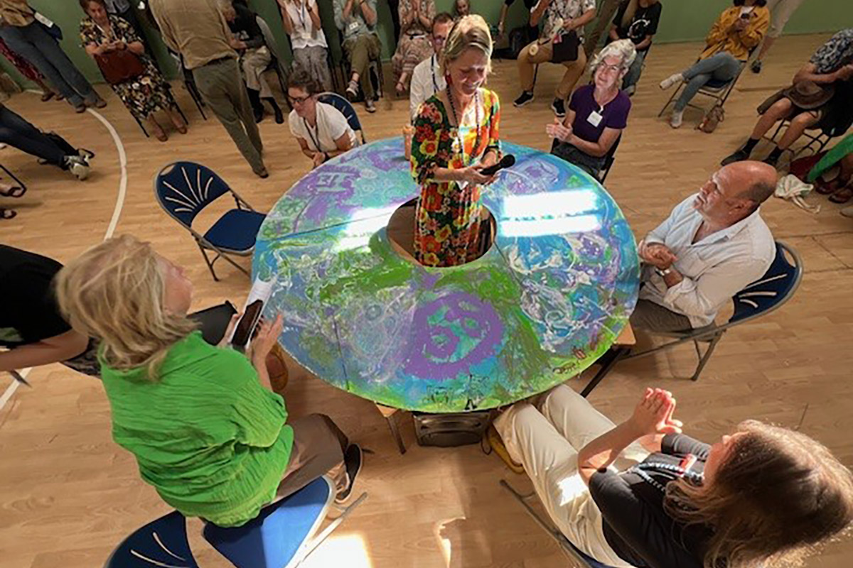 Image shows woman in centre of round table with people sitting around her