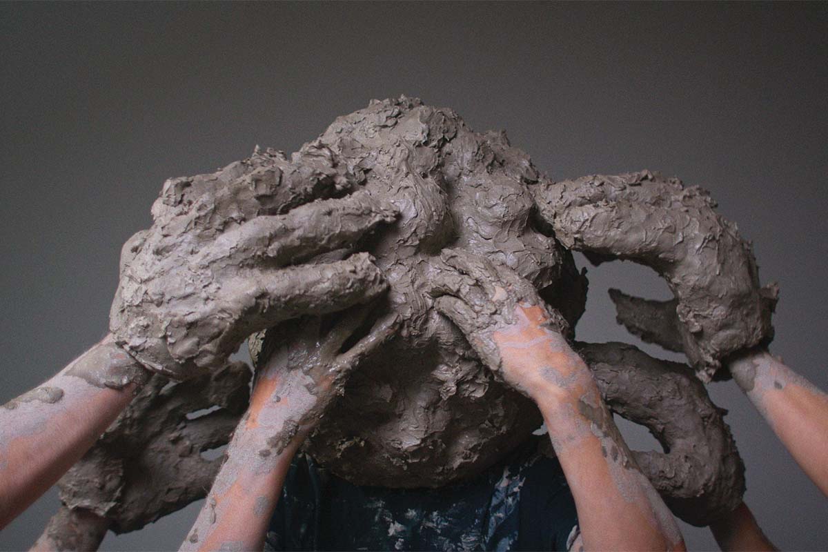 Image shows hands rubbing clay on a person's head, Mess of help (2023) by William Cobbing