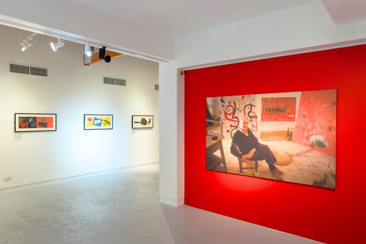 Photo of Joan Miró exhibition, large photograph of Joan Miró on a red wall and three smaller lithographs